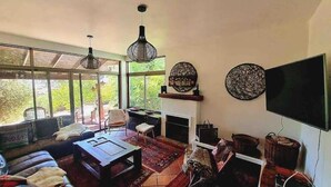 Ein Wohnzimmer mit Kamin, großen Fenstern und einem Fernseher.