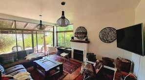 Ein Wohnzimmer mit Kamin, großen Fenstern und einem Fernseher.