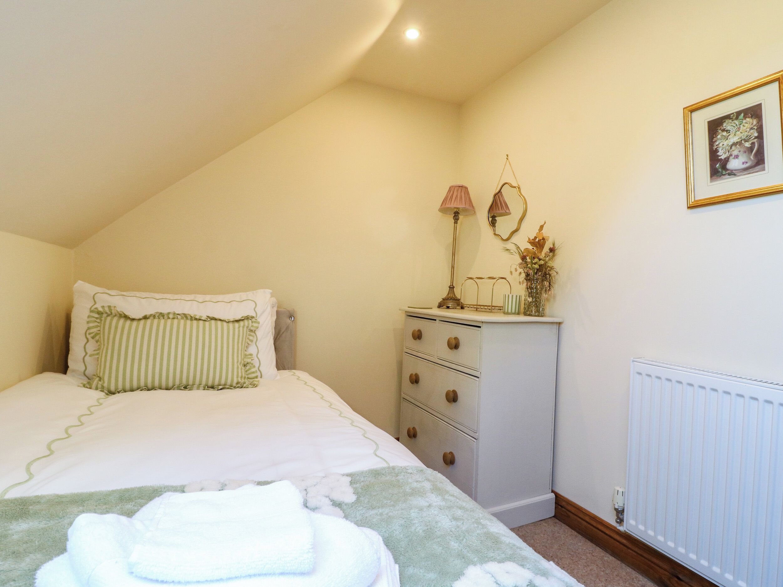 Un dormitorio con cama, cómoda, radiador y lámpara de pared.