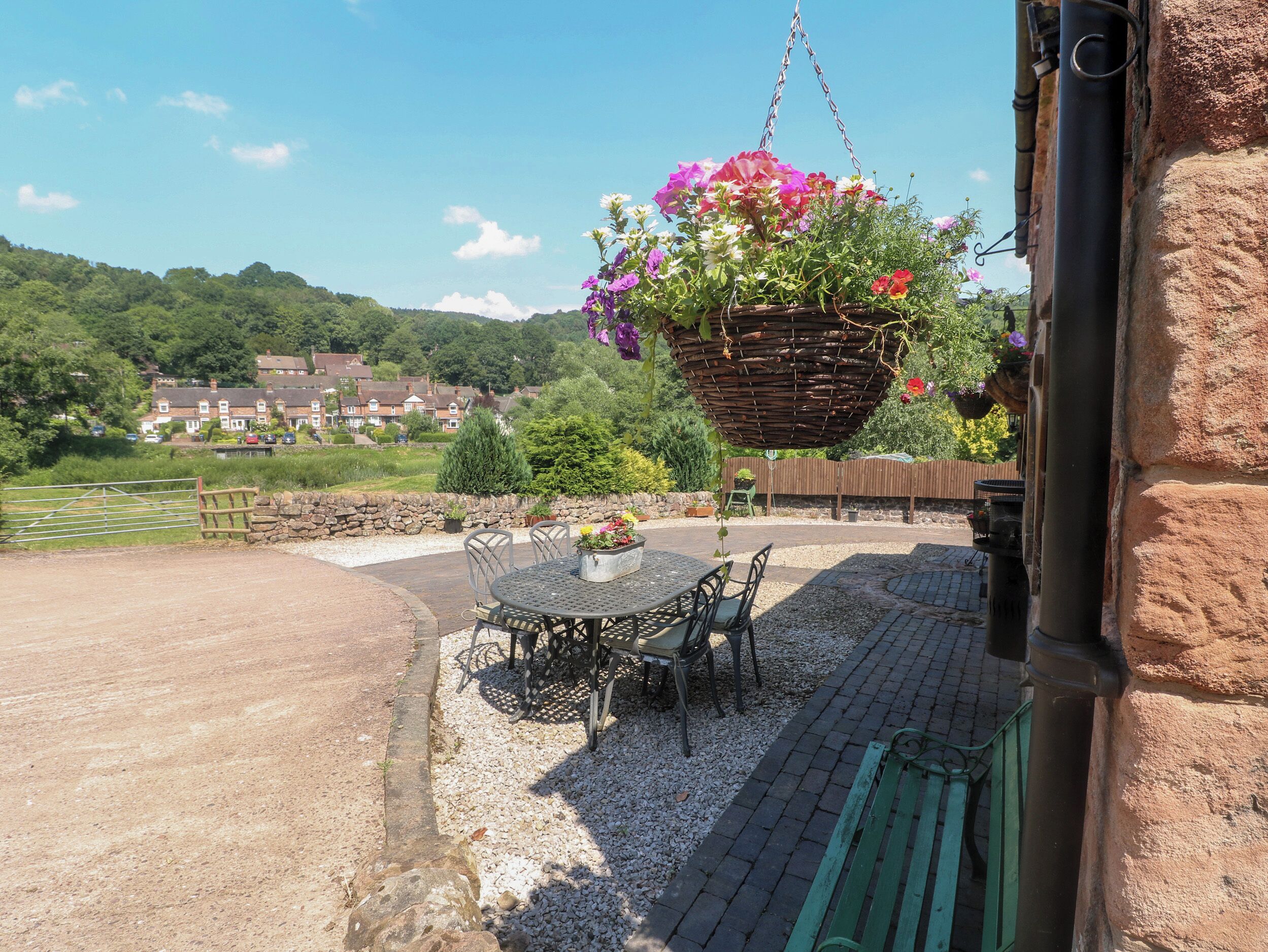 Un patio con mesa y sillas, una cesta colgante de flores y vistas a casas al fondo.