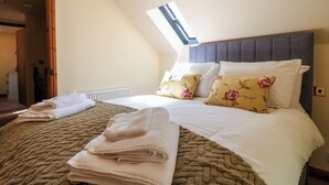 Un dormitorio con techo inclinado, una cama con almohadas florales, un radiador y un tragaluz.