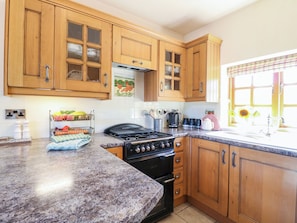 A kitchen with wooden cabinets, a gas stove, a sink, and a window with a view. - Bluebell Barn (Stoke-on-Trent)
