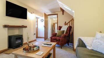 Una sala de estar con chimenea, televisor, sofá, un sillón rojo y una mesa de centro de madera.