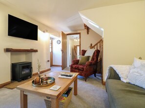 Una sala de estar con chimenea, televisor, sofá, un sillón rojo y una mesa de centro de madera.