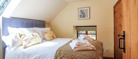 A bedroom with a bed, pillows, a blanket, a window, and a door.