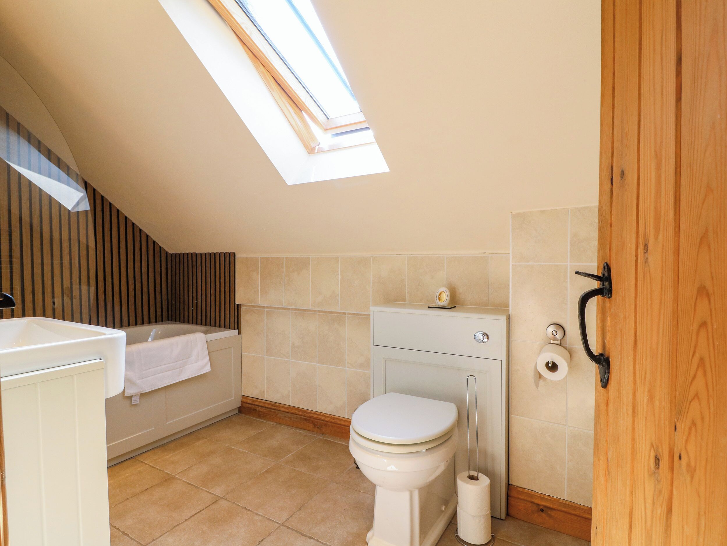 A small, modern bathroom with a skylight, a toilet, a bathtub, and a wooden door.