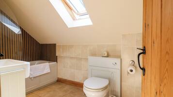 A small, modern bathroom with a skylight, a toilet, a bathtub, and a wooden door.