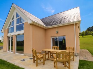 A two-story house with a patio area featuring a wooden table and chairs.