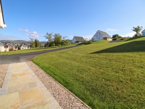 A residential area with houses, a paved driveway, and a grassy hill.