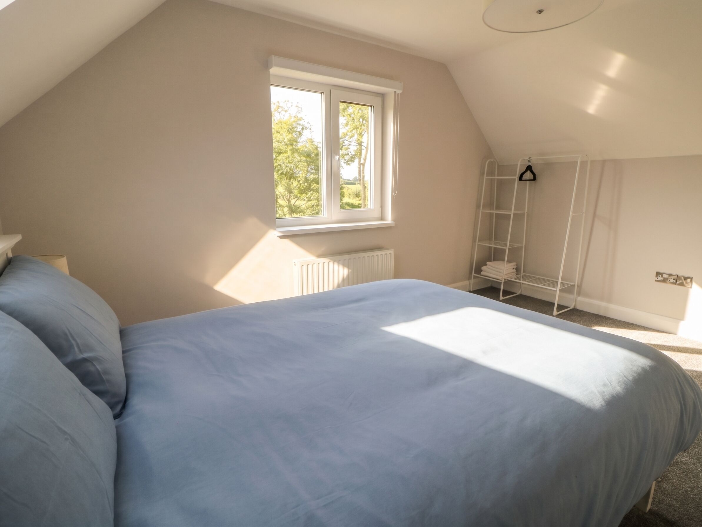 A bedroom with a bed, a window, a radiator, and a white metal shelf.