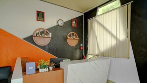 A reception desk with a white marble top, two wooden shelves with decorative items, a clock, and a window with blinds. - Lima Residence Cozy Double (Bandar Lampung)