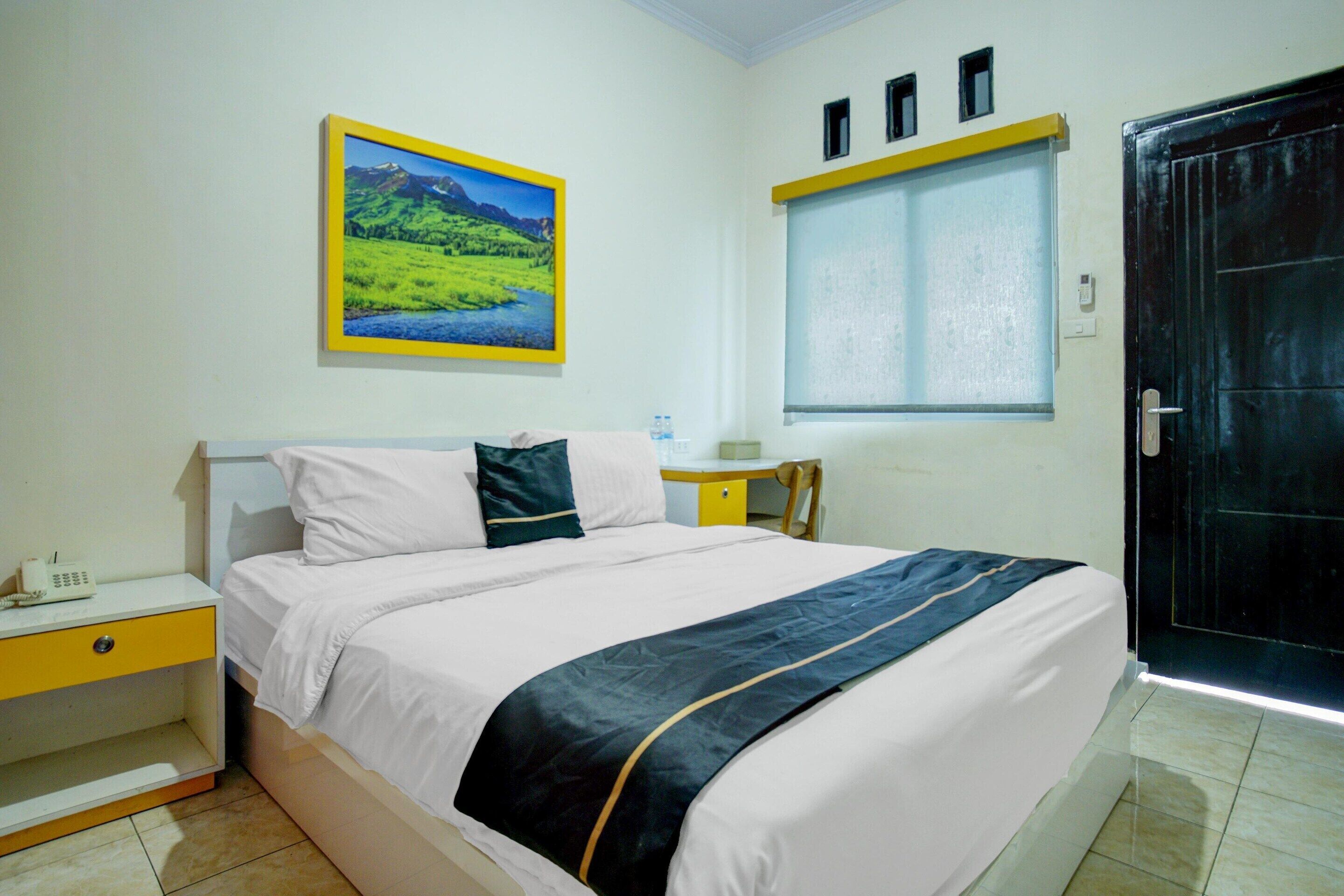 A hotel room with a bed, a nightstand, a desk, a window, and a door.