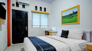 A hotel room with a bed, a desk, a chair, a window with blinds, a door, and a framed picture on the wall. - Lima Residence Cozy Double (Bandar Lampung)
