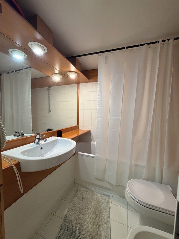 A bathroom with a sink, mirror, shower curtain, and toilet.