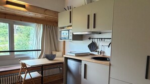 A compact kitchen with a built-in dishwasher, a window with curtains, and a radiator under a wooden table.