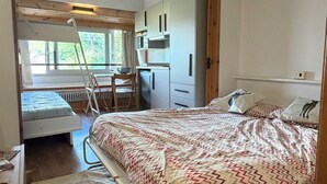A bedroom with a bed, a desk, a chair, a radiator, and a window.