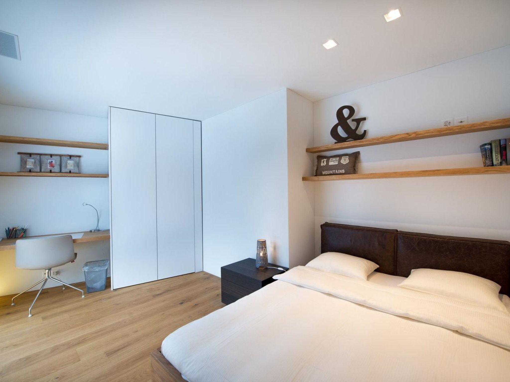 A modern bedroom with a bed, bedside table, and a desk with a chair.