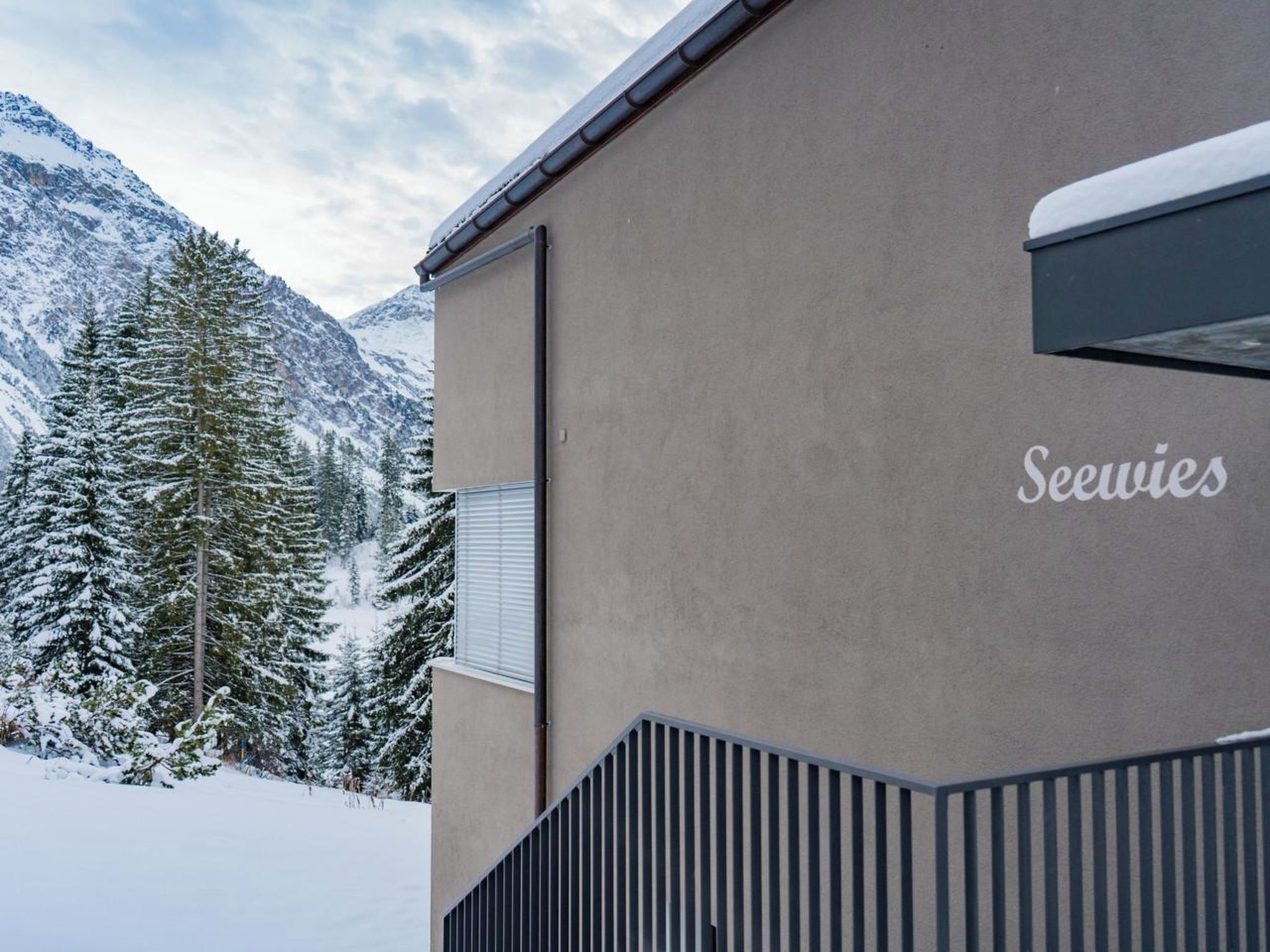 Ein Gebäude mit einem 'Seewies' Schild, umgeben von schneebedeckten Bergen und Bäumen.