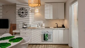 A modern kitchen with white cabinetry, a clock, a hanging light fixture, and a window with blinds. - Large Holiday Home, Jacuzzi, Sauna (Choczewo)