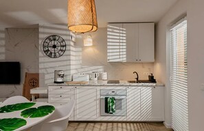 A modern kitchen with white cabinetry, a clock, a hanging light fixture, and a window with blinds. - Large Holiday Home, Jacuzzi, Sauna (Choczewo)