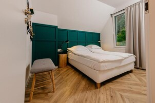 Un dormitorio con cama, mesita de noche, lámpara, ventana con cortinas y suelo de madera.