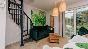 Una sala moderna con una escalera, un sofá verde, un cofre de madera y vistas a través de un ventanal.