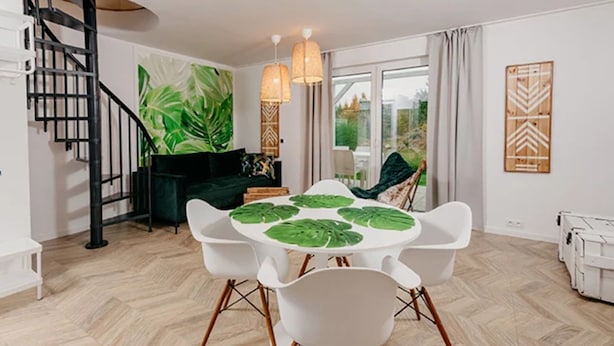 A dining area with a round table, white chairs, a green sofa, a staircase, and a large window. - Large Holiday Home, Jacuzzi, Sauna (Choczewo)