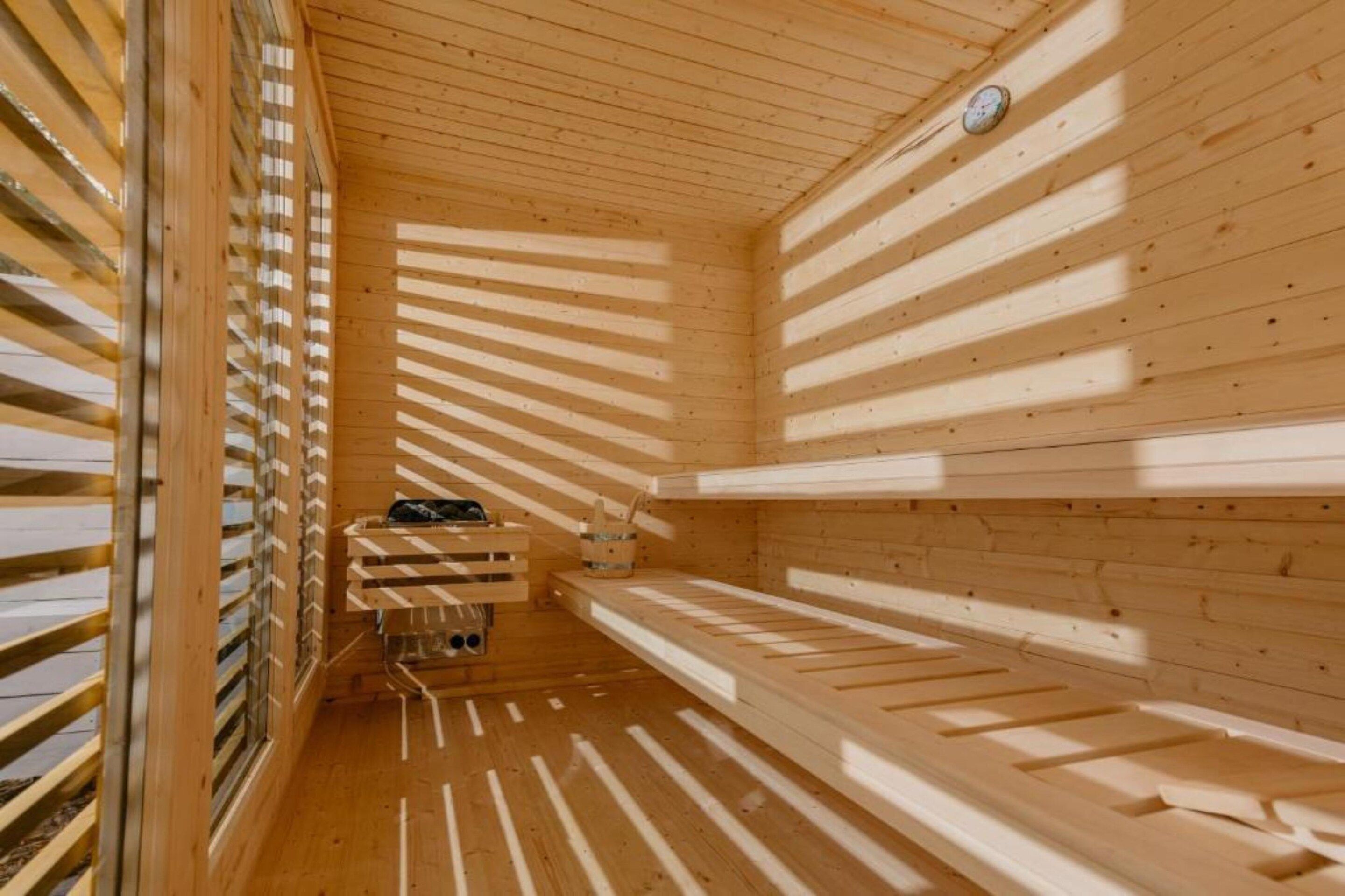 Una sauna con listones de madera en las paredes y el techo, un banco y una pequeña mesa con un cubo.