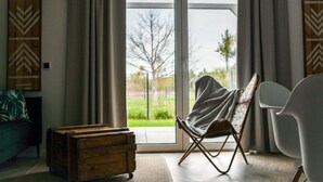 A modern living room with a large sliding glass door, a wooden chest, a folding chair, and a white chair. - Large Holiday Home, Jacuzzi, Sauna (Choczewo)