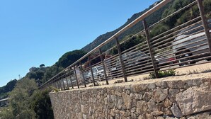 Un muro di pietra con ringhiera metallica che si affaccia su un'area di parcheggio e un paesaggio montuoso.