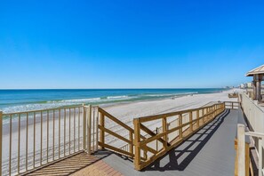 Ein hölzerner Steg führt zu einem Strand mit blauem Himmel.