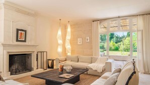 Una sala de estar con chimenea, un juego de sofás, una mesa de centro y vistas al exterior con vegetación.