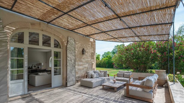 Un patio exterior con zona de estar cubierta, un muro de piedra y vistas a un jardín.