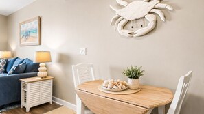 Un coin repas avec une table en bois, des chaises blanches, une plante en pot et un élément décoratif en forme de crabe accroché au mur.