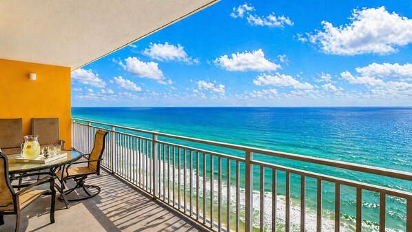 A balcony with a table and chairs, overlooking a turquoise sea and clear sky. - Splash Into Paradise | Gulf-Front 20th Floor Retreat at Splash Resort (Panama City Beach)