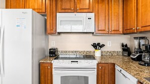 Une cuisine avec des meubles de rangement en bois, un réfrigérateur blanc, un four à micro-ondes, une cuisinière, un grille-pain et un mixeur.