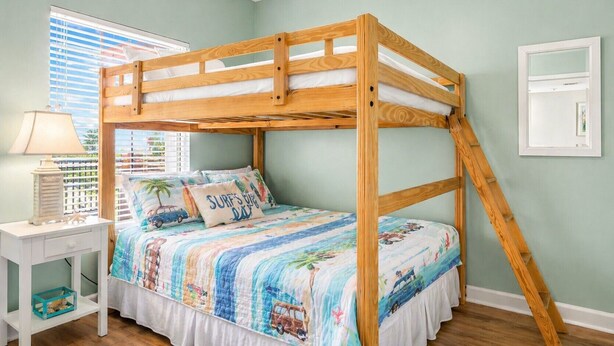 Un lit superposé avec une structure en bois, un matelas blanc et une couverture colorée sur le thème de la plage.