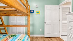 Un lit superposé avec une couvre-lit aux couleurs vives, une porte blanche et une commode à tiroirs.