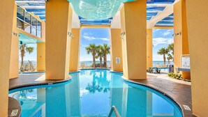 Une piscine intérieure à l’eau d’un bleu cristallin, entourée de murs et de piliers jaunes, avec vue sur l’océan et les palmiers.