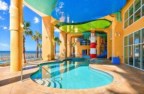 Un espace piscine avec vue sur l’océan, une tour de surveillance pour les sauveteurs et une aire de jeux pour enfants.