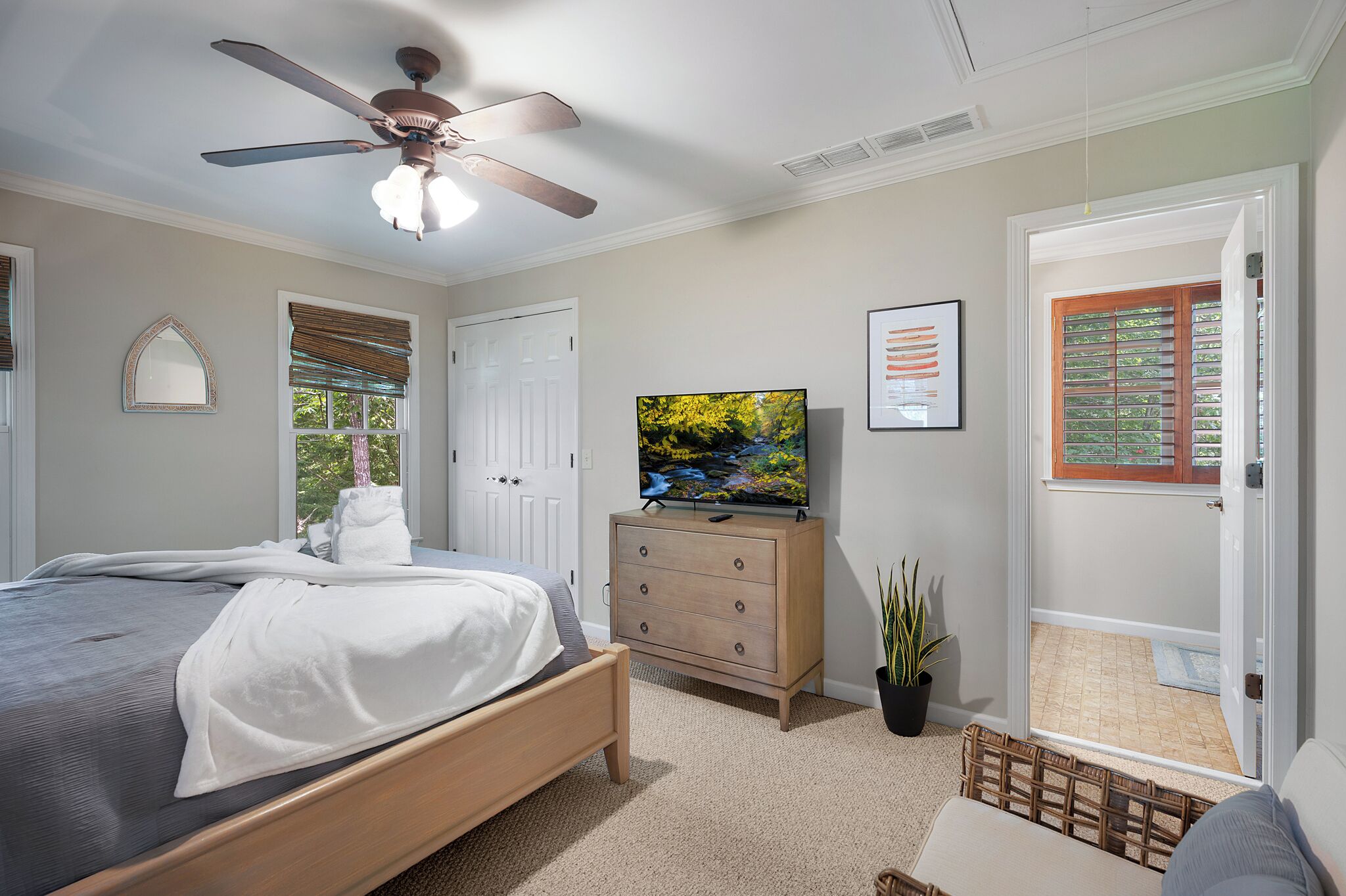 A bedroom with a bed, a dresser, a television, a ceiling fan, and a door leading to a balcony.