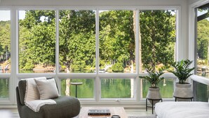 Ein Zimmer mit großem Fenster, einer Couch, einem Bett, einem Couchtisch mit Büchern und zwei Zimmerpflanzen.