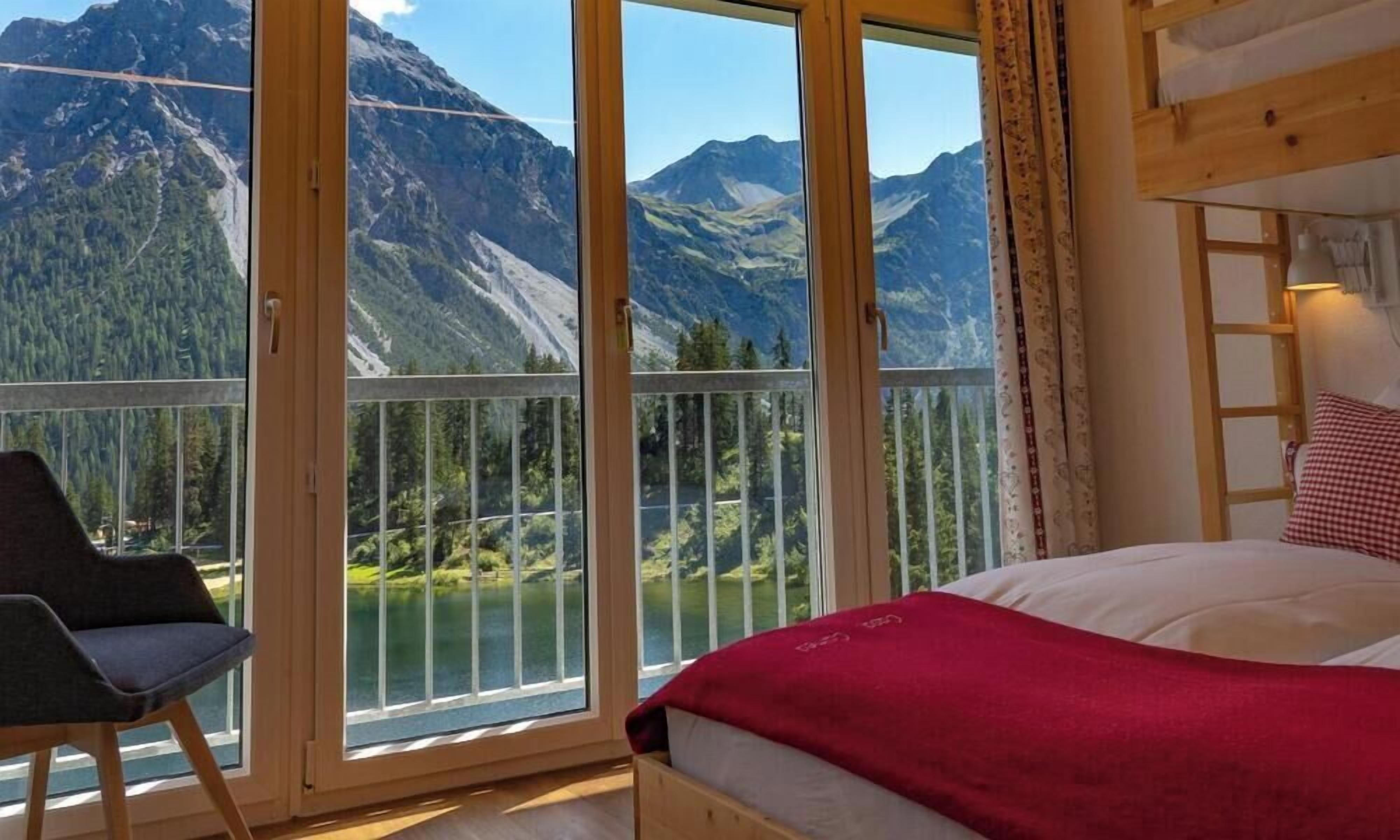Ein Schlafzimmer mit großem Fenster mit Blick auf einen See und Berge, einem Stockbett und einem Stuhl.