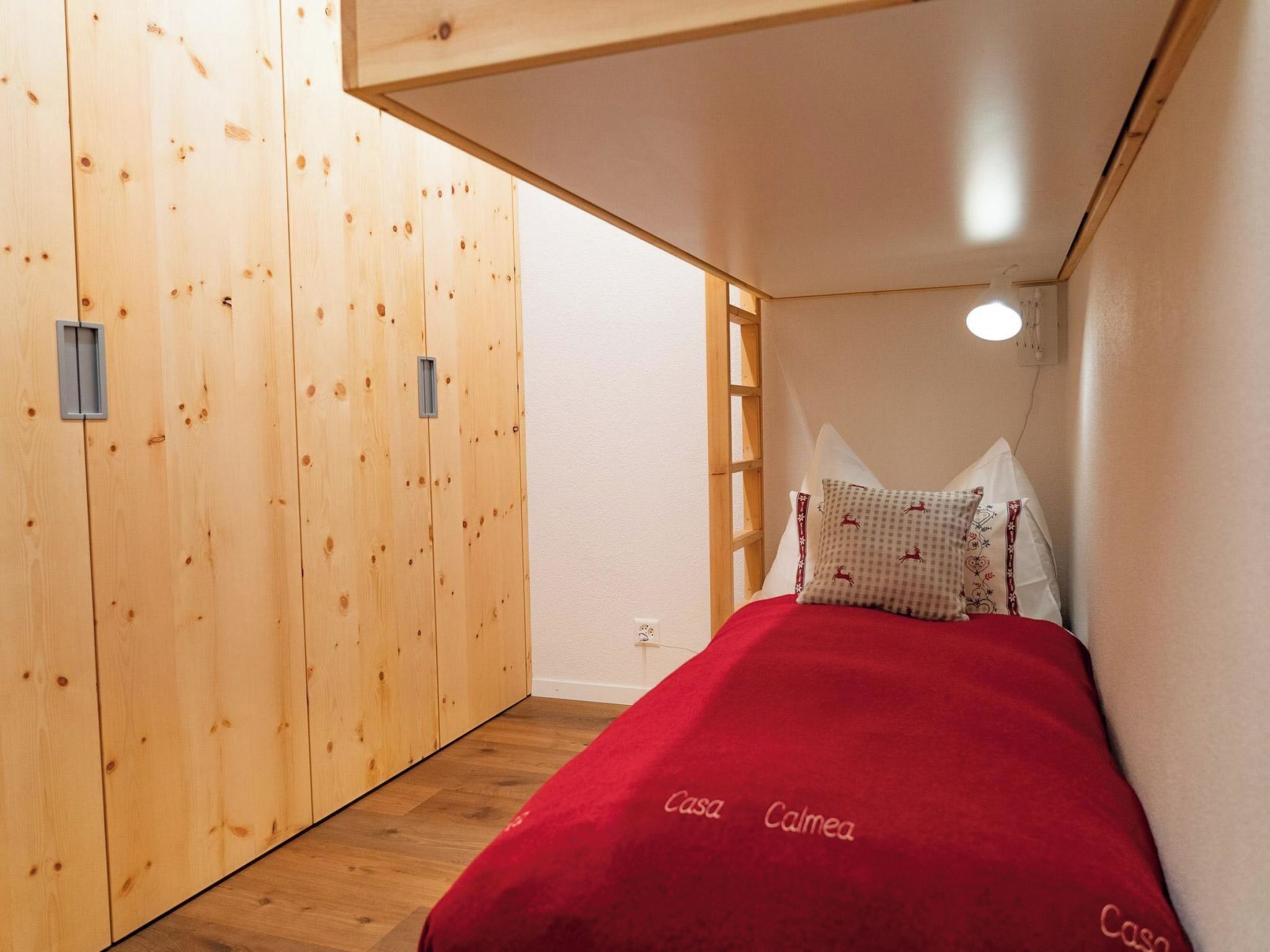 Una camera da letto con un'armadiatura in legno, un letto con cuscini decorati e una scala appoggiata al muro.