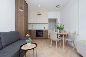 Eine moderne Küche mit Holzschränken, einem Esstisch mit Stühlen, einer Couch und einem kleinen Beistelltisch mit einer Pflanze.