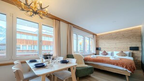 Une chambre moderne avec un coin repas, un lit doté d’une tête de lit en bois et de grandes fenêtres.