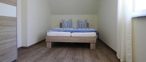 A bedroom with a wooden bed, white walls, and a window with curtains.