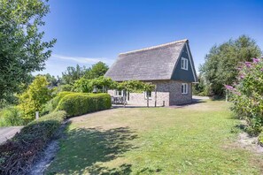 A house with a stone exterior, a thatched roof, and a well-maintained lawn. - Lavish 4-person Beach Villa in Makkum (Makkum)