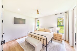 Ein Schlafzimmer mit einem Bett, Nachttischen, einer Bank, einem Deckenventilator, einem Fernseher und einem Fenster mit Vorhängen.