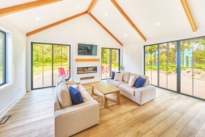 A spacious living area with a high ceiling, large windows, and a fireplace. - Beach House w/ Patio & Game Room (CoastalC) (Long Beach)
